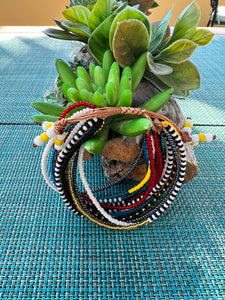 The Shanga Slide Beaded Bracelet by Her Best Foot Forward, inspired by Maasai jewelry, adds vibrant color to your look. Handmade in East Africa, this easy slip-on bracelet shines beside green succulents on a blue woven mat.