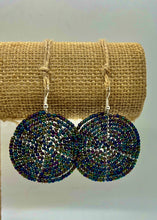 Load image into Gallery viewer, The Duara Circular Beaded Earrings by Her Best Foot Forward—handmade Maasai statement jewelry from East Africa—feature round, multicolored beads on hooks, displayed on a textured burlap stand against a plain light background.