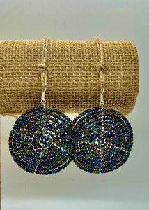 The Duara Circular Beaded Earrings by Her Best Foot Forward—handmade Maasai statement jewelry from East Africa—feature round, multicolored beads on hooks, displayed on a textured burlap stand against a plain light background.