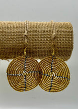 Load image into Gallery viewer, The Duara Circular Beaded Earrings by Her Best Foot Forward are large, gold wire Maasai statement earrings with black and white accents, shown hanging on a burlap stand against a plain background.