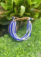 Load image into Gallery viewer, The Shanga Slide Beaded Bracelet by Her Best Foot Forward is an easy slip-on Maasai-inspired piece featuring blue, white, and silver beads displayed on green artificial grass with leafy plants behind.