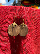 Load image into Gallery viewer, The Rosemiti Hand-Carved Rosewood Earrings by Her Best Foot Forward, accented with brass, are displayed against vibrant red fabric and colorful patterns, reflecting the rich heritage of East African statement jewelry.