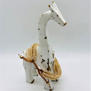 A white, distressed wooden giraffe figurine stands on a plain background, adorned with the Shanga Slide Beaded Bracelet by Her Best Foot Forward—an easy slip-on Maasai-inspired jewelry piece from East Africa.