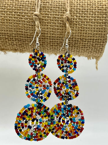 The Kiungo Conjoined Circle Earrings by Her Best Foot Forward are handmade Maasai statement jewelry from East Africa, featuring small, colorful beads in three linked circles, displayed against a textured burlap background.