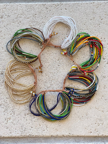 The Shanga Slide Beaded Bracelet by Her Best Foot Forward showcases Maasai-inspired, colorful beads in unique combinations—white, gold, green, blue, red, yellow, and black—artfully arranged in a circular pattern on textured stone.