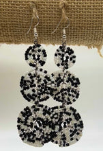 Load image into Gallery viewer, The Kiungo Conjoined Circle Earrings by Her Best Foot Forward are handmade Maasai statement earrings featuring black and white concentric circles, hanging from silver hooks—unique East African jewelry displayed on burlap fabric.