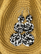 Load image into Gallery viewer, The Kiungo Conjoined Circle Earrings by Her Best Foot Forward are handmade Maasai statement earrings from East Africa, featuring black and white beads in spiral patterns, shown on a woven tan basket background.